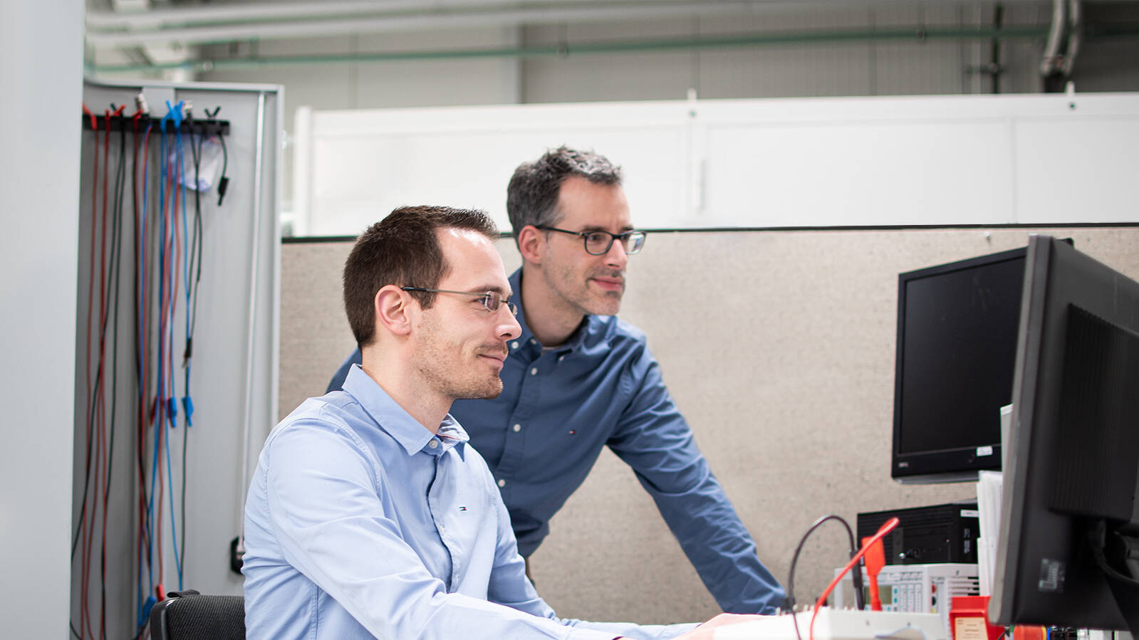 Two men at a desk look into a screen together