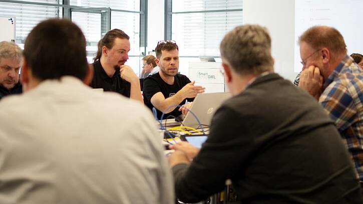 a group of men sitting around a table and working on laptops with and other electronic devices