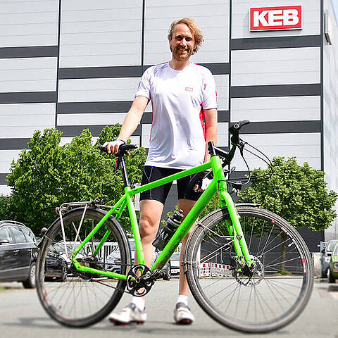 A man with a bicycle in front of a KEB building