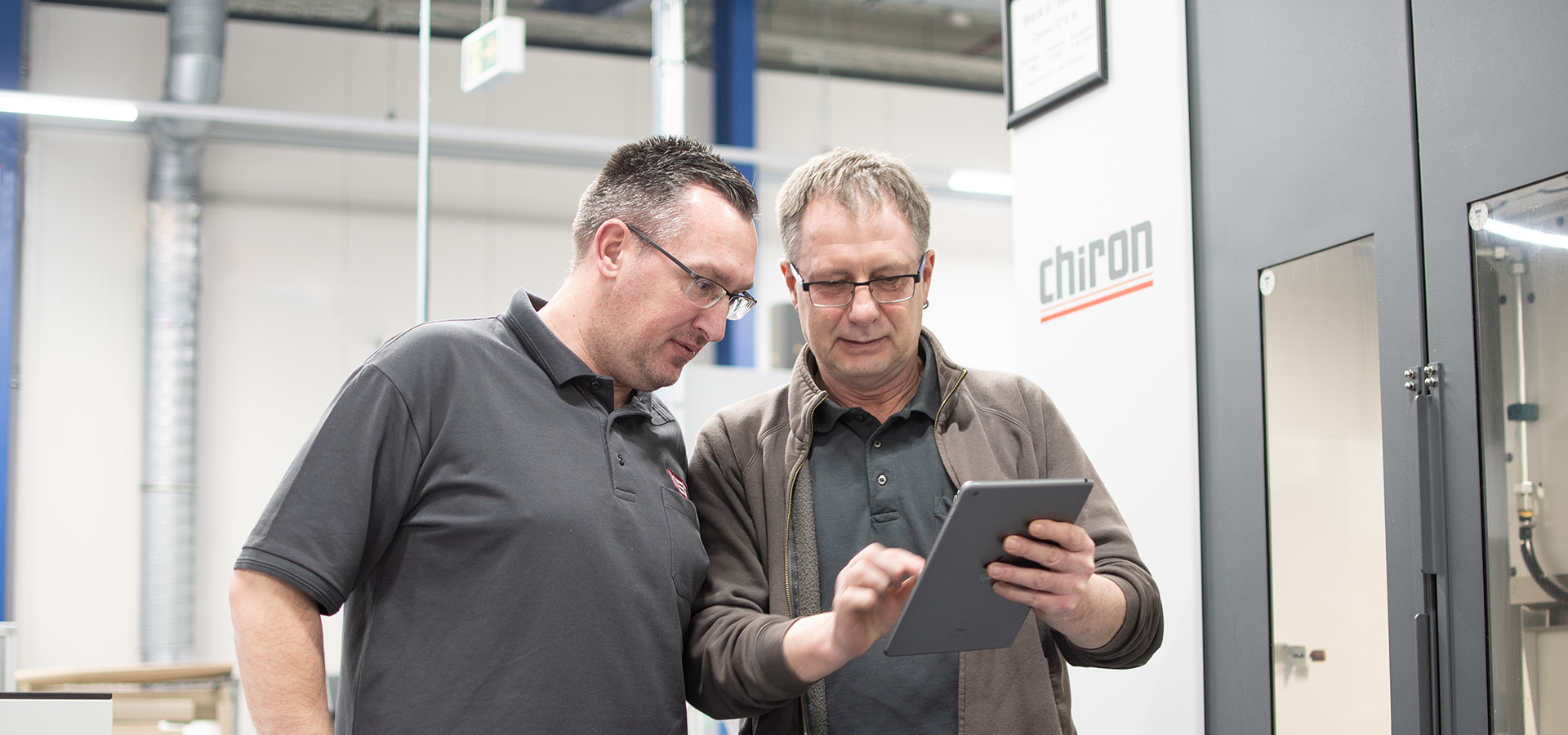 Zwei Männer stehen vor einer Maschine und schauen gemeinsam in ein Tablet